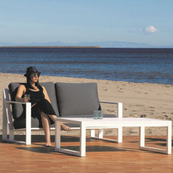 En una playa, sofá de 2 plazas blanco con chica y cojines grises